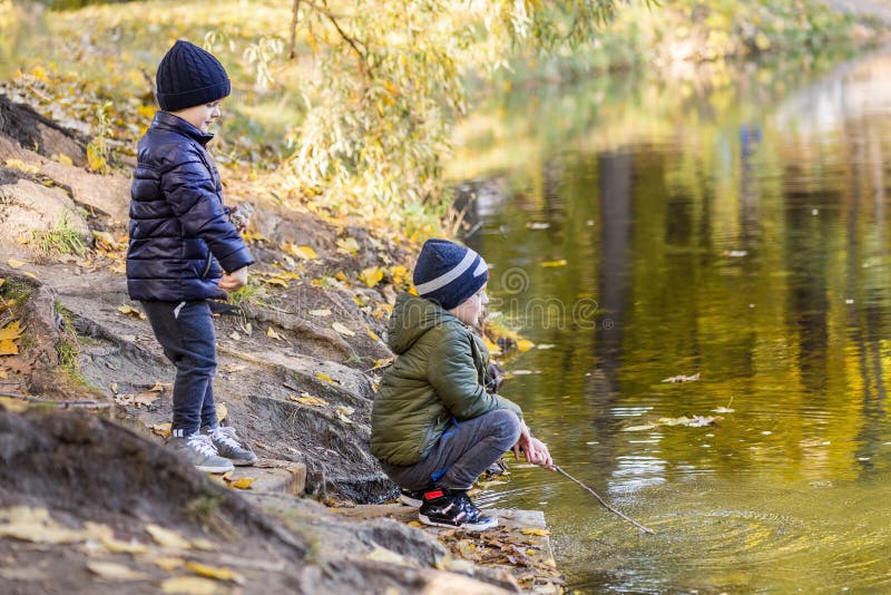 Two young boys playing fishing with sticks near pond in fall park. Little brothers having fun near lake or river in autumn. Happy