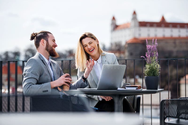 Two young business people with laptop sitting on a terrace outside office, working.