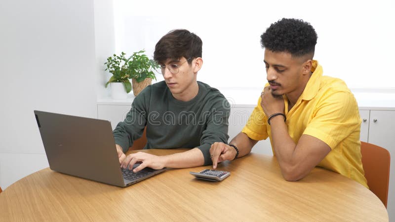 Two young businessmen collaborating on a laptop at a modern office stock video footage