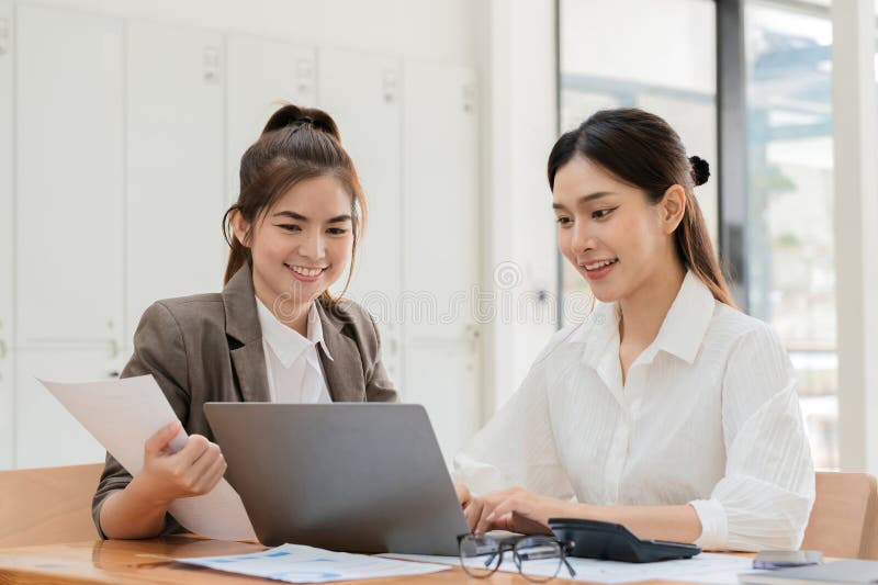 Young Businesswoman and Colleague Collaborating on Project in Modern Office Setting with Documents and Laptop, Smiling stock photography