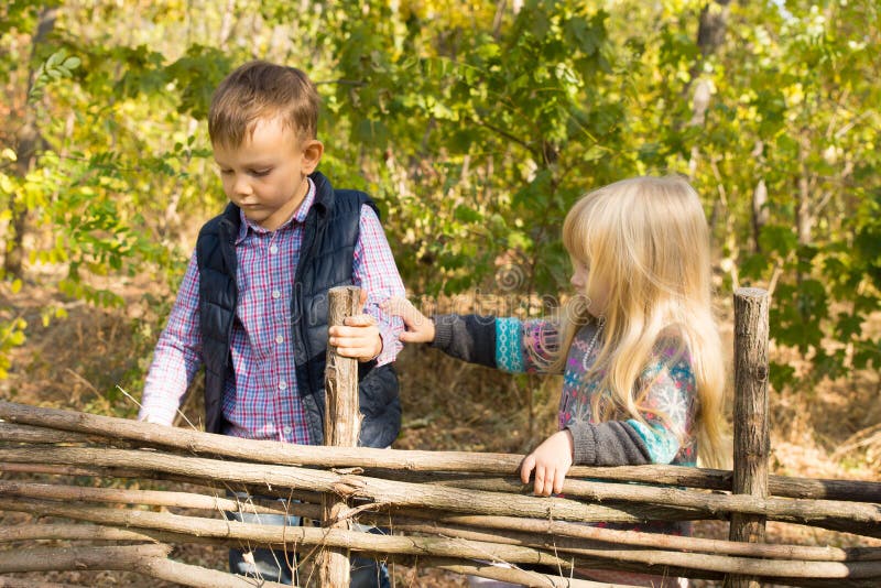 Two young children playing at a wooden fence