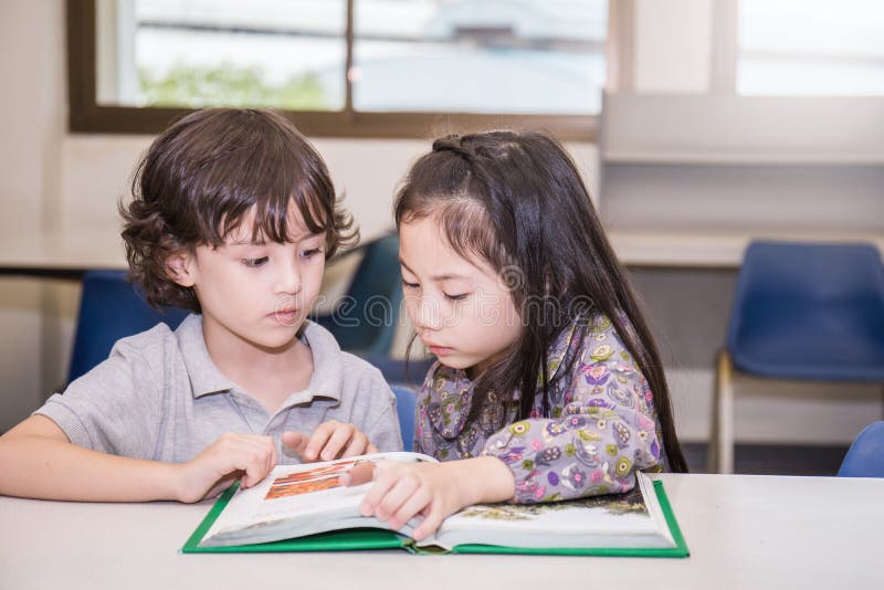 Two young children reading books at the school library, Education concept