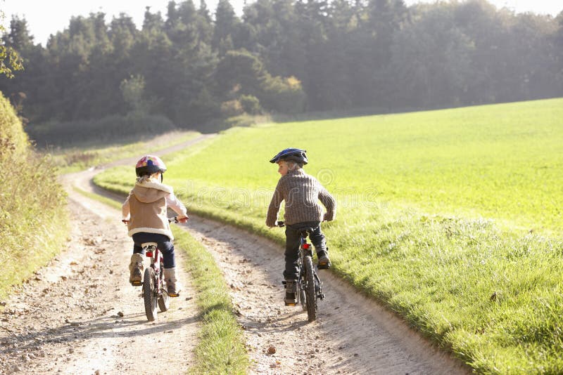 Two young children ride bicycles in park back view