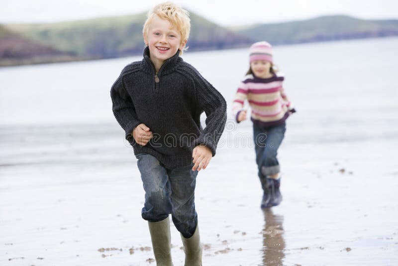 Two young children running on beach smiling.