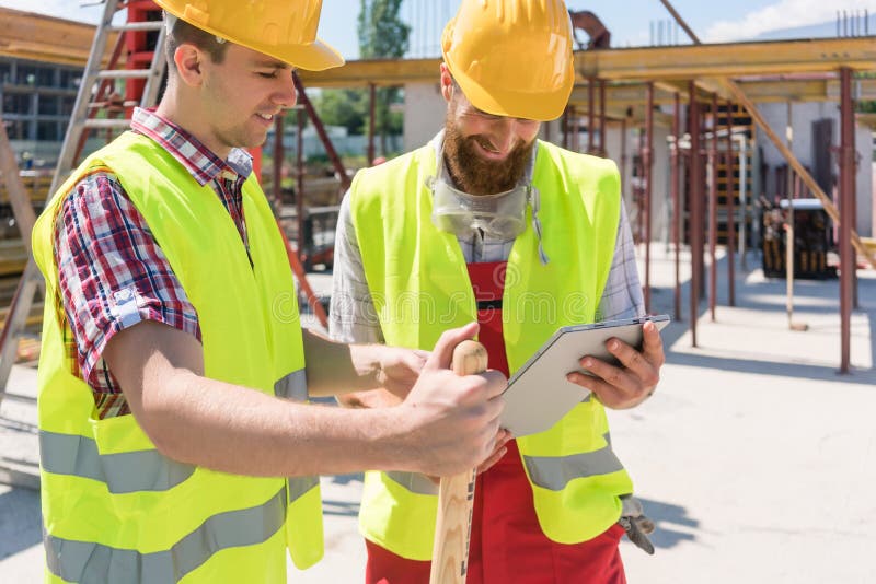 Two young construction workers smiling while using a tablet duri stock photo