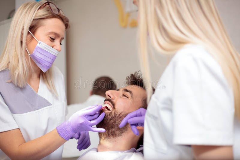 Two young female dentists working in dental clinic. Whitening male patient`s teeth and using tone chart to mach color royalty free stock images Two young female dentists working in dental clinic. Whitening male patient`s teeth and using tone chart to mach color royalty free stock images