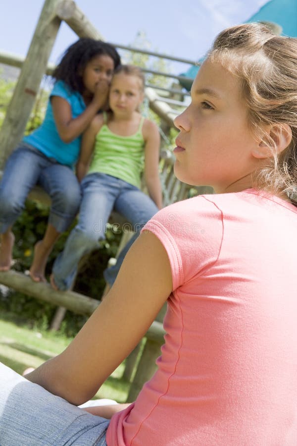 Dva mladí dívka přátelé na hřiště šušká o jiné dívce.