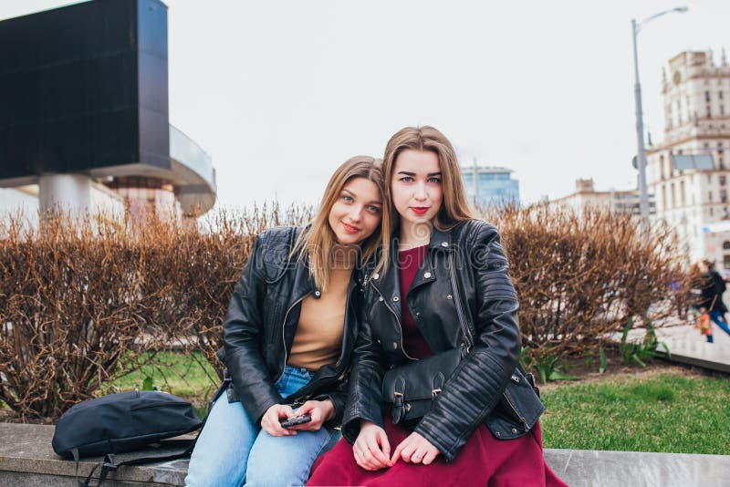 Two young girl friends sitting together and having fun in city .Outdoors. lifestyle.