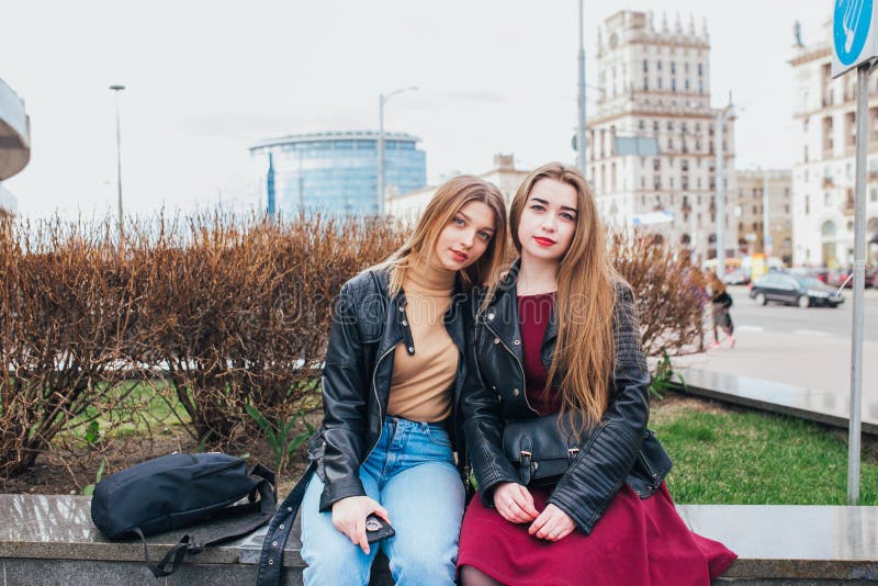 Two young girl friends sitting together and having fun in city .Outdoors. lifestyle.