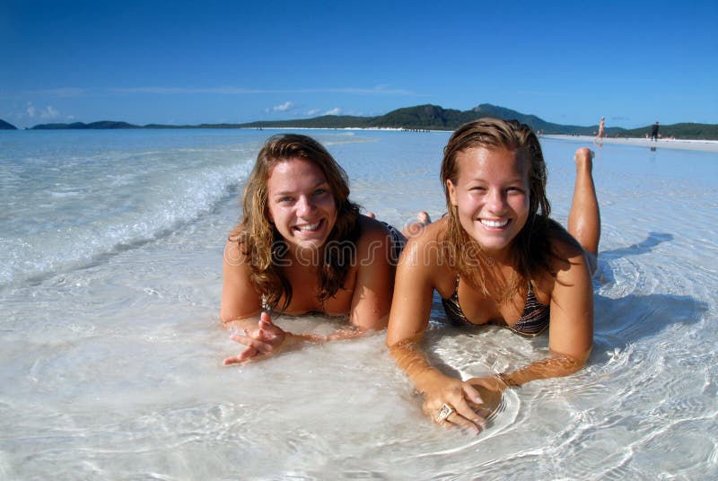 Two young girls in bikini laying in the water