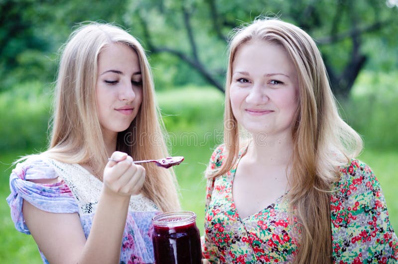 Two young happy young women eating strawberry jam on summer green outdoors background