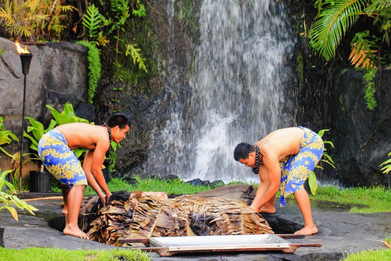 Two young Hawaiian men uplift a cooked pig