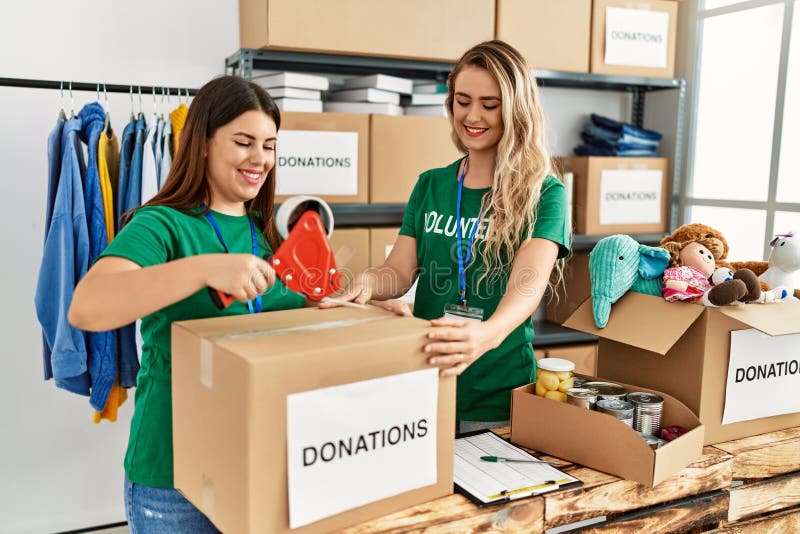 Two young volunteers woman smiling happy packing donations box at charity center