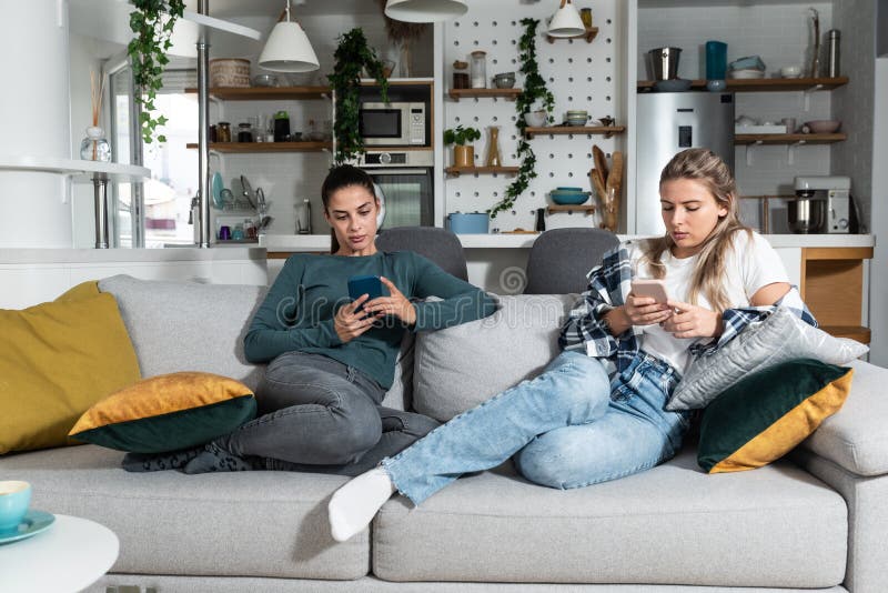Two young woman lesbian couple roommates sitting on the sofa at home angry after argue not talking. Females addiction to internet stock photos