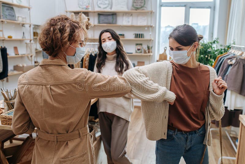 Two young women in an ecological shop greeting each other, touching elbows