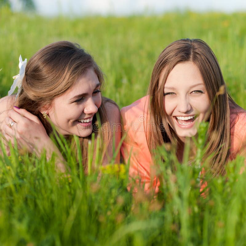 Two Teen Girl Friends Laughing having fun in green grass on summer day. Two Teen Girl Friends Laughing having fun in green grass on summer day