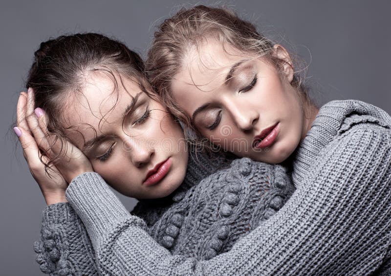 Two young women in gray sweaters on grey background. Beautiful g stock photo Two young women in gray sweaters on grey background. Beautiful g stock photo