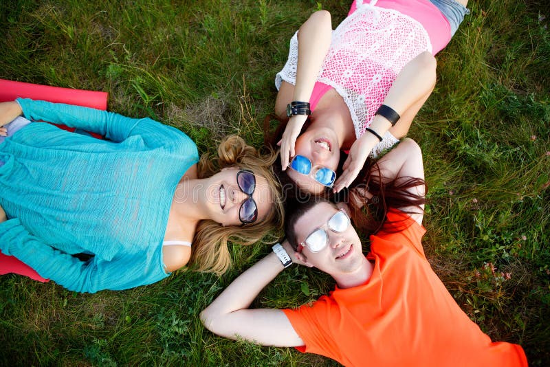 Two young women and man resting while lying on grass stock photo Two young women and man resting while lying on grass stock photo