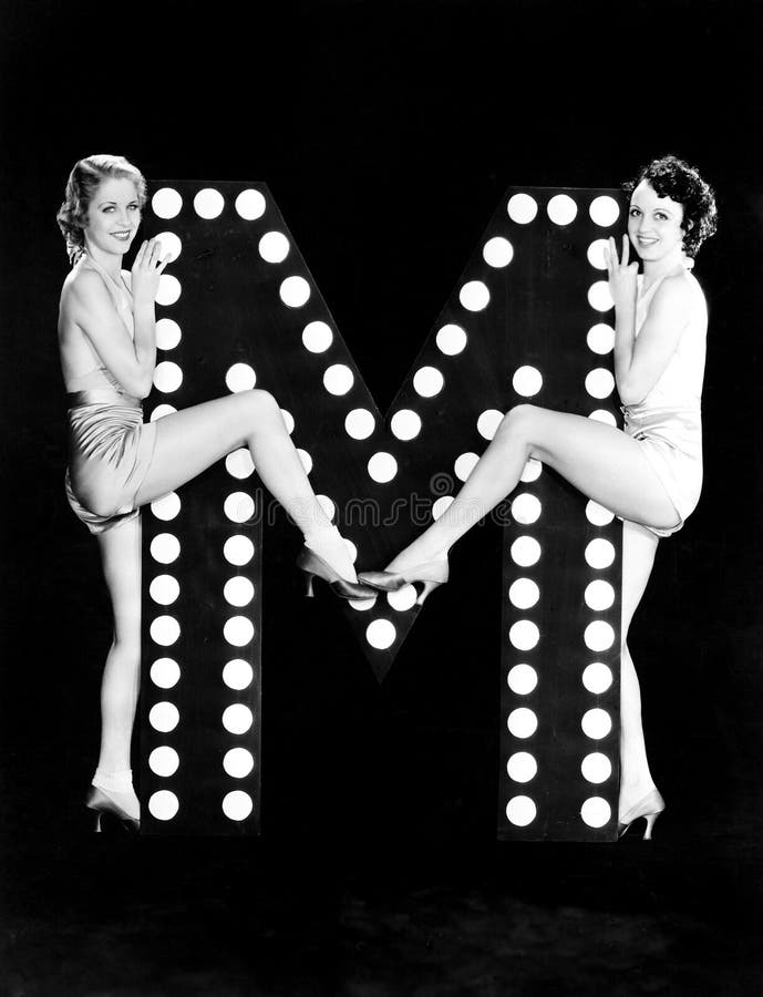Two young women posing with the letter M