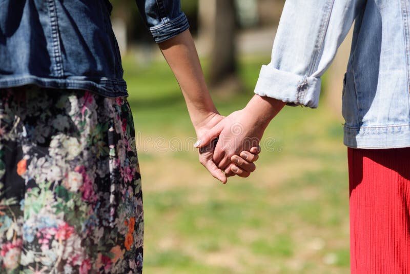 Two young women in walking holding her hands in urban park.