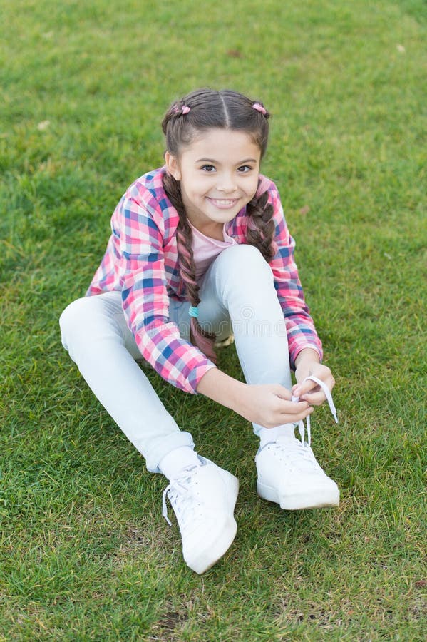 Tying shoelaces. Girl little kid spend leisure outdoors in park. Girl sit on grass in park. Child enjoy spring sunny