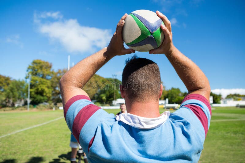 Tylni widok rugby gracza mienia piłka podczas gdy stojący przy trawiastym polem zdjęcia royalty free Tylni widok rugby gracza mienia piłka podczas gdy stojący przy trawiastym polem zdjęcia royalty free