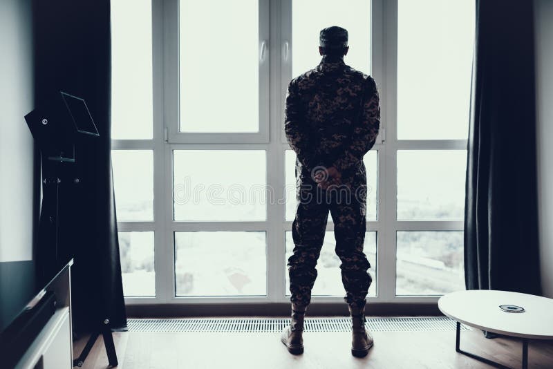 Tylny widok mężczyzna w wojskowym uniformu Blisko okno zdjęcia stock