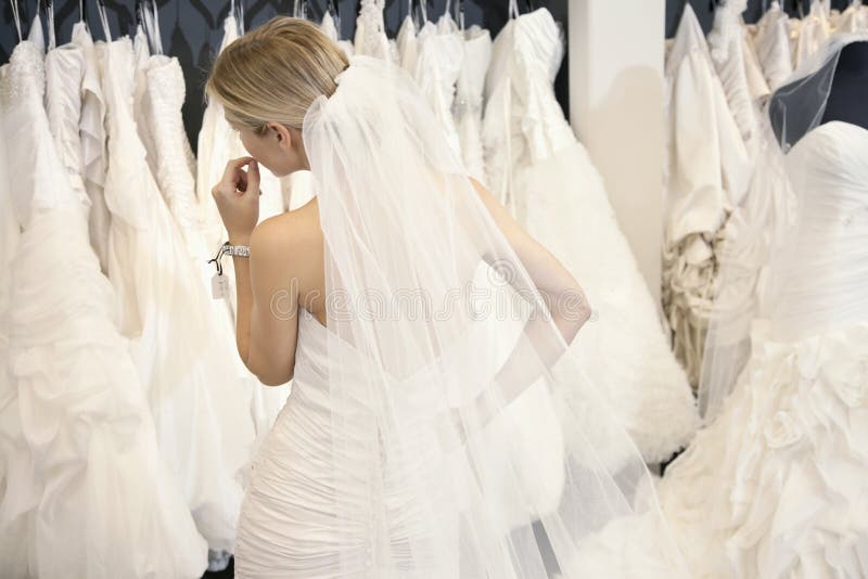 Tylny widok młoda kobieta patrzeje bridal togi na pokazie w butiku w ślubnej sukni