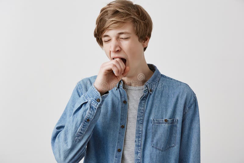 Type blond dans la chemise de denim semblant fatiguée et somnolente, baîllement, couvrant la bouche de, après nuit sans sommeil m photo stock Type blond dans la chemise de denim semblant fatiguée et somnolente, baîllement, couvrant la bouche de, après nuit sans sommeil m photo stock