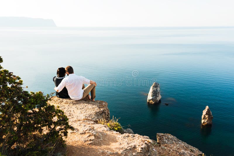Type et fille s'asseyant au bord d'une falaise par la mer image libre de droits Type et fille s'asseyant au bord d'une falaise par la mer image libre de droits