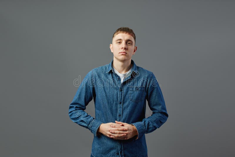 Type habillé dans un T-shirt blanc, les jeans et la chemise de jeans se tenant avec ses bras pliés dans le studio sur le fond gri photos stock Type habillé dans un T-shirt blanc, les jeans et la chemise de jeans se tenant avec ses bras pliés dans le studio sur le fond gri photos stock