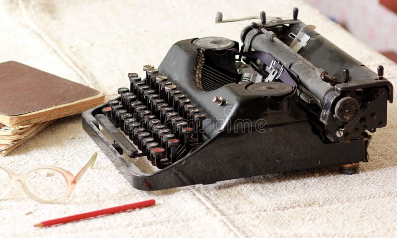 Type noir auteur en métal de vintage à côté d'une pile de vieux carnets, des paires de lunettes et d'un crayon sur une nappe de t photos stock Type noir auteur en métal de vintage à côté d'une pile de vieux carnets, des paires de lunettes et d'un crayon sur une nappe de t photos stock