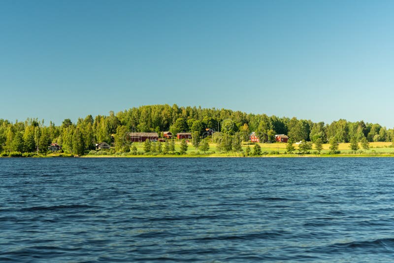 Typical Swedish countryside farm located by a lake with green fields and surrounding forest. On a beautiful summer day with clear blue sky and sunshine making the whole environment glow. Typical Swedish countryside farm located by a lake with green fields and surrounding forest. On a beautiful summer day with clear blue sky and sunshine making the whole environment glow
