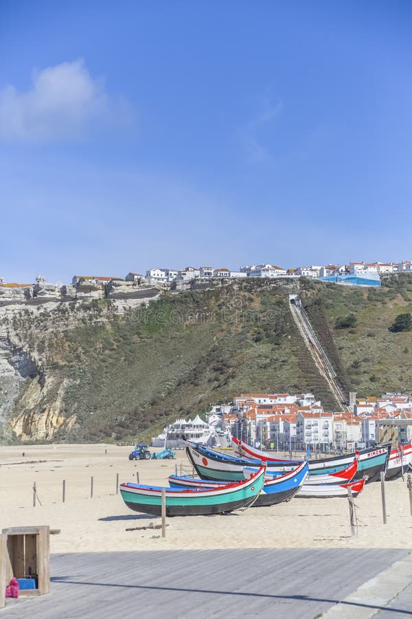 Typical view at the Nazare beach with colored and traditional fishing boats and cliff with funicular lift and the city on top as 库存图片 Typical view at the Nazare beach with colored and traditional fishing boats and cliff with funicular lift and the city on top as 库存图片