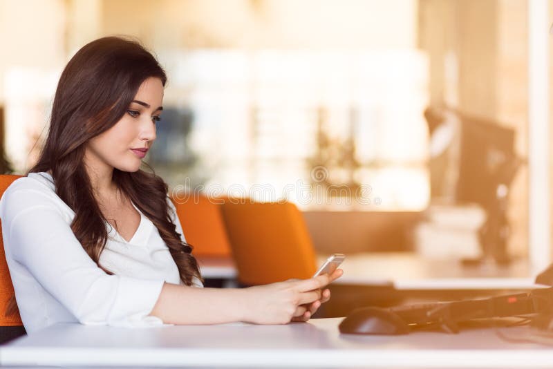 Typing business message. Confident young woman in smart casual wear holding smart phone and looking at it with smile royalty free stock photography Typing business message. Confident young woman in smart casual wear holding smart phone and looking at it with smile royalty free stock photography