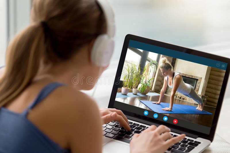 Back view of millennial girl relax at home enjoy yoga online training practice course on laptop, young woman watch fitness sports workout video using modern internet application on computer. Back view of millennial girl relax at home enjoy yoga online training practice course on laptop, young woman watch fitness sports workout video using modern internet application on computer