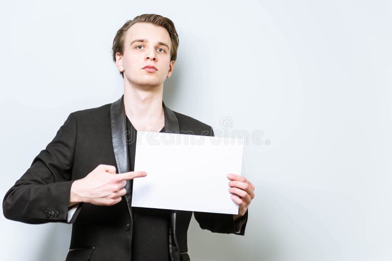 Tânăr om de afaceri cu cămașă neagră și blazer, care ține un panou alb și care arată cu degetul spre el. afaceri stock photos