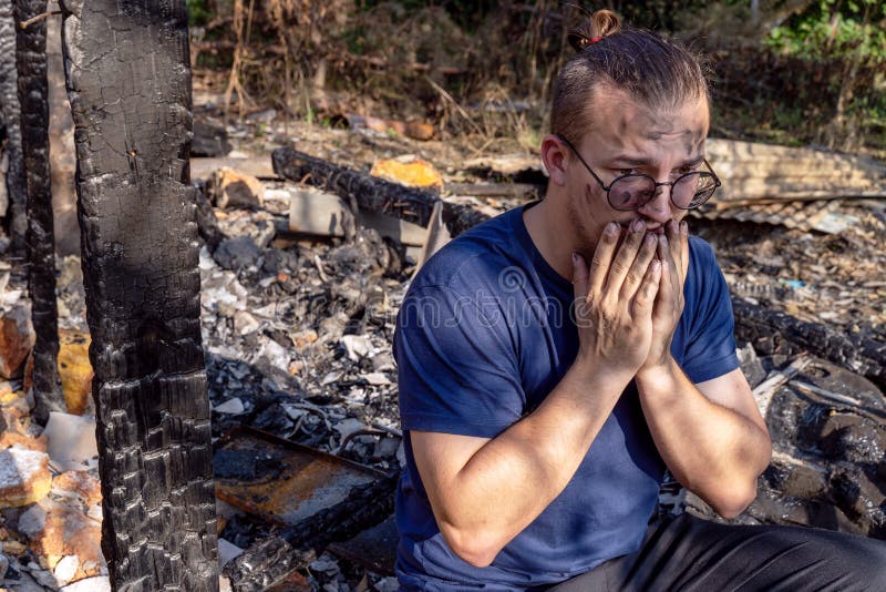 Tânărul stă pe ruinele casei distruse cu foc. stock image