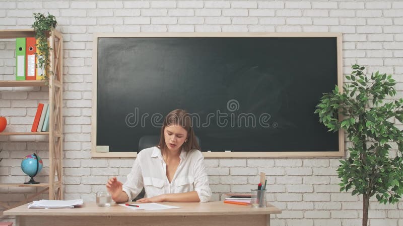 Tânără femeie profesor de colegiu la birou în sala de clasă în fața hârtiilor de testare a notării tablei de cretă expresie stresa stock footage