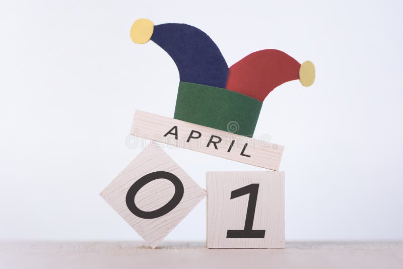 Fools` Day, date April 1 on wooden calendar and clown cap on a white background. Fools` Day, date April 1 on wooden calendar and clown cap on a white background