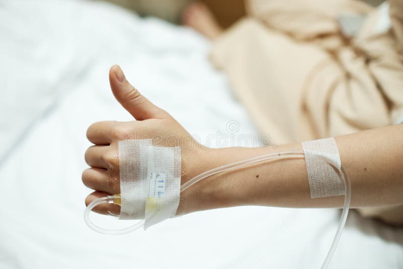 Tålmodiga handtummar upp medan given salthaltig droppdroppandeinjektion på sjukhussäng arkivfoto Tålmodiga handtummar upp medan given salthaltig droppdroppandeinjektion på sjukhussäng arkivfoto