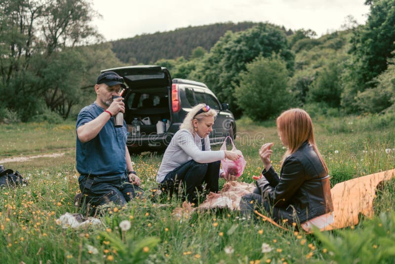 Tè felice pranzare e della bevanda della famiglia campeggio, fine settimana, picnic uomo, donna, ragazza, incrocio, automobile di fotografia stock Tè felice pranzare e della bevanda della famiglia campeggio, fine settimana, picnic uomo, donna, ragazza, incrocio, automobile di fotografia stock