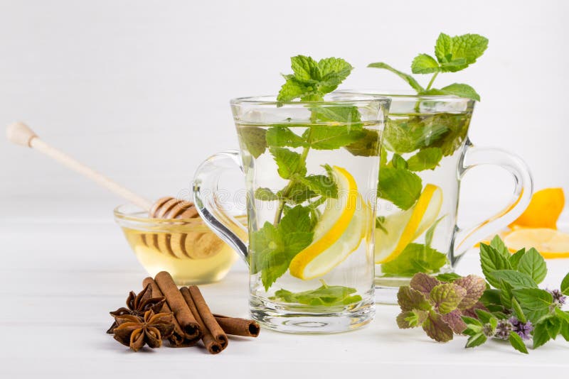 Té de cristal de la menta fresca de dos tazas con el limón y la miel en el fondo blanco fotos de archivo Té de cristal de la menta fresca de dos tazas con el limón y la miel en el fondo blanco fotos de archivo