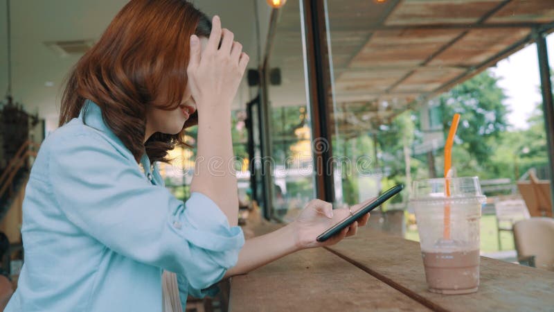 Té verde helado de consumición que se sienta asiático feliz alegre de la mujer joven en café usando el smartphone para hablar, la almacen de video
