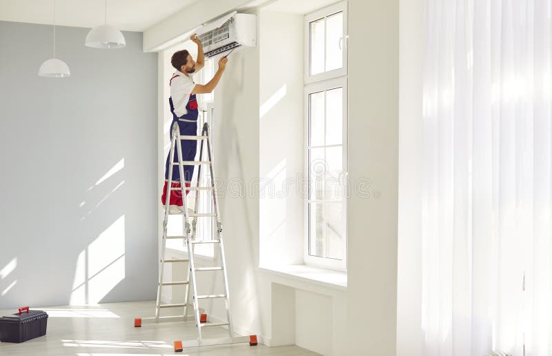 Técnico profesional masculino instalando un aire acondicionado de pared moderno en una casa nueva. imagen de archivo libre de regalías