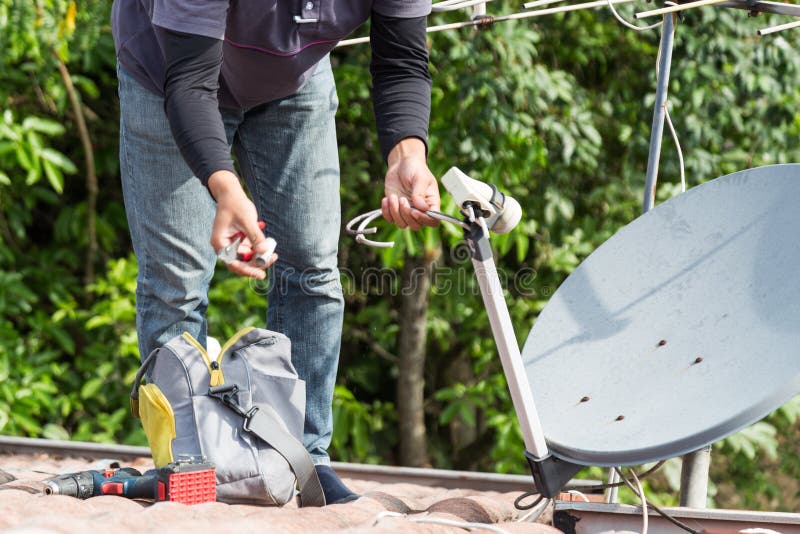 Técnico que instala la antena de la antena parabólica y de televisión en el top del tejado fotografía de archivo Técnico que instala la antena de la antena parabólica y de televisión en el top del tejado fotografía de archivo