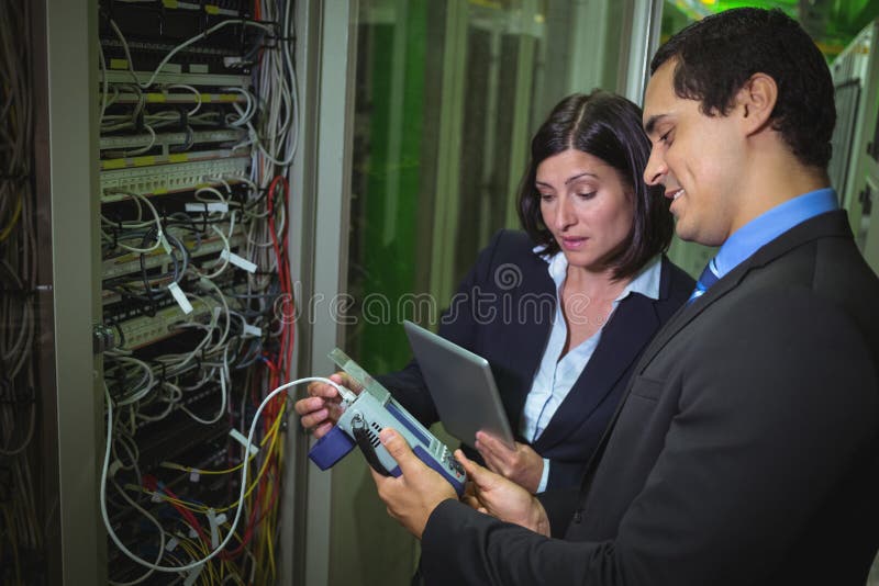 Técnico que trabalha no computador pessoal ao analisar os técnicos do servidor que usam o cabo digital analy foto de stock Técnico que trabalha no computador pessoal ao analisar os técnicos do servidor que usam o cabo digital analy foto de stock