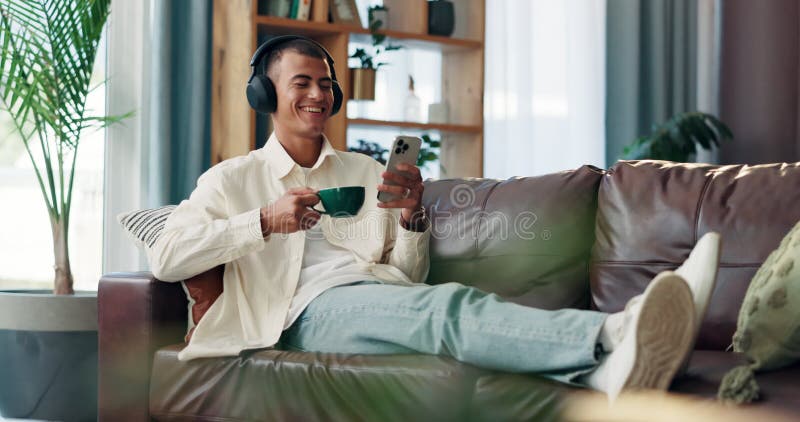 Téléphone café et homme avec casque sur canapé le matin regarder ou drôle vidéo en ligne à la maison. Rire relax et mâle banque de vidéos