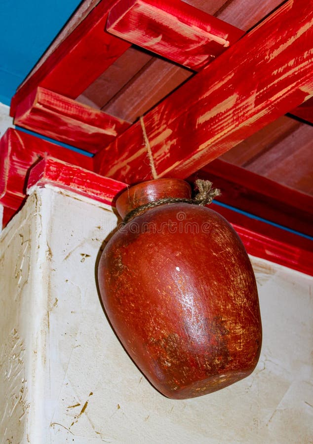 Töpferwarentopf, der durch Seil von den roten Dachsparren gegen weiße Stuckwand hängt stockbild Töpferwarentopf, der durch Seil von den roten Dachsparren gegen weiße Stuckwand hängt stockbild
