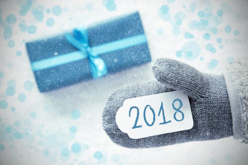 Glove With Label With Text 2018 For Happy New Year. Turquoise Gift Or Present On Snow In Background. Seasonal Greeting Card With Snowflakes And Bokeh Effect. Glove With Label With Text 2018 For Happy New Year. Turquoise Gift Or Present On Snow In Background. Seasonal Greeting Card With Snowflakes And Bokeh Effect